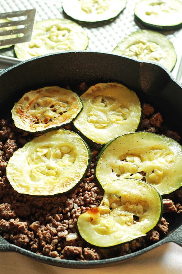 Zucchini slices layered on top of ground beef in a pan