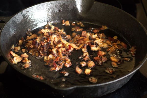 Pieces of bacon cooking in a skillet