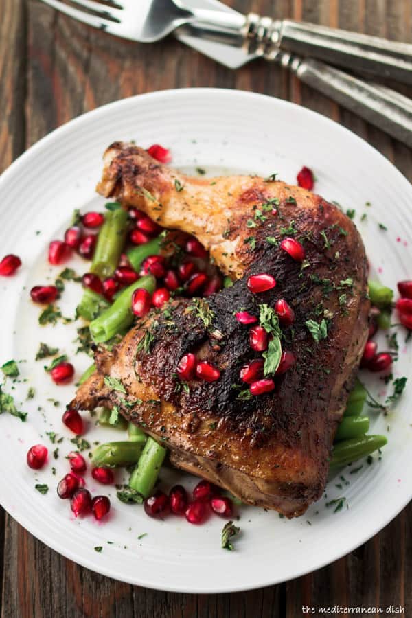 Pomegranate chicken thigh served on a plate garnished with extra pomegranate seeds