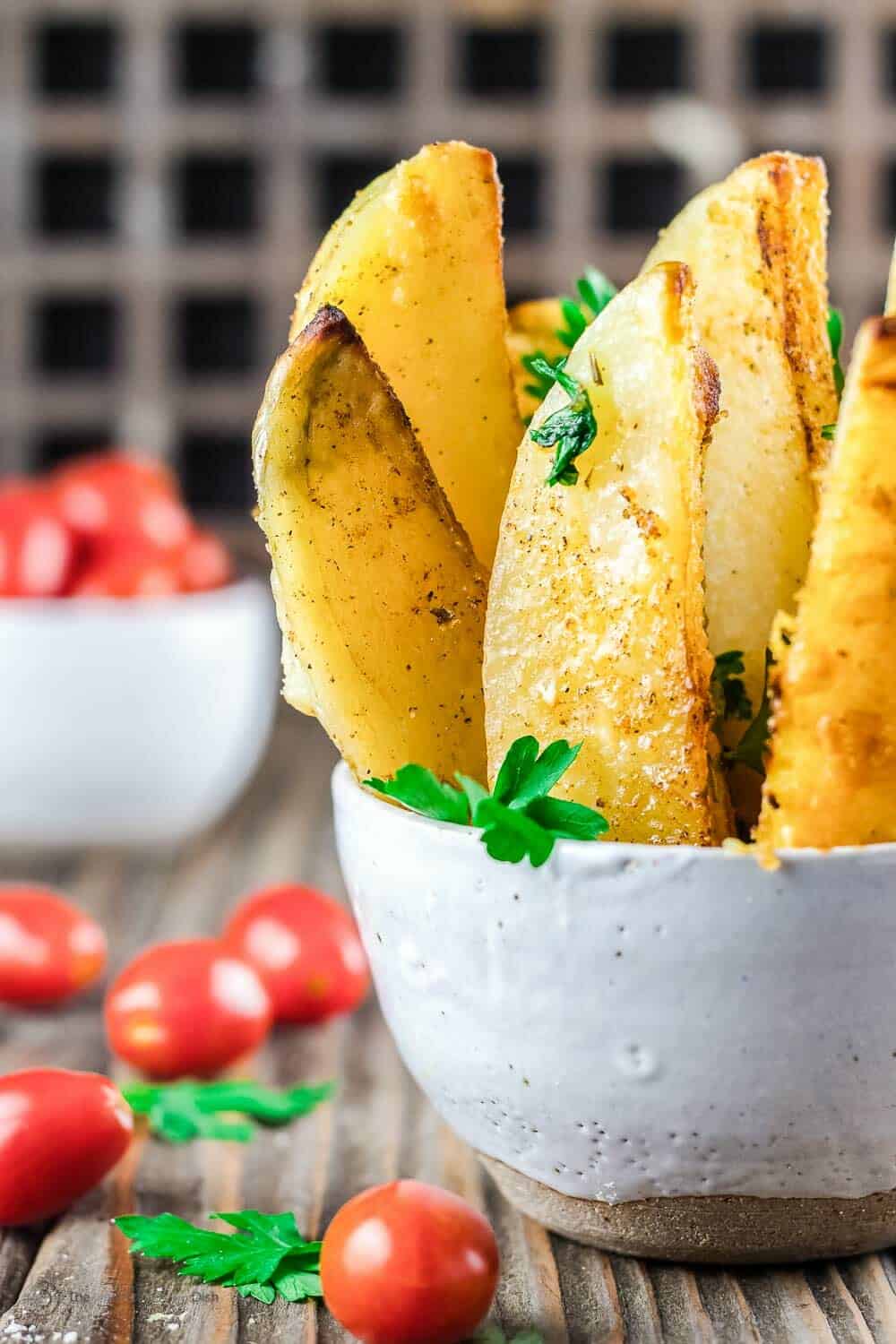roasted greek potato wedges topped with parsley in a bowl next to cherry tomatoes.
