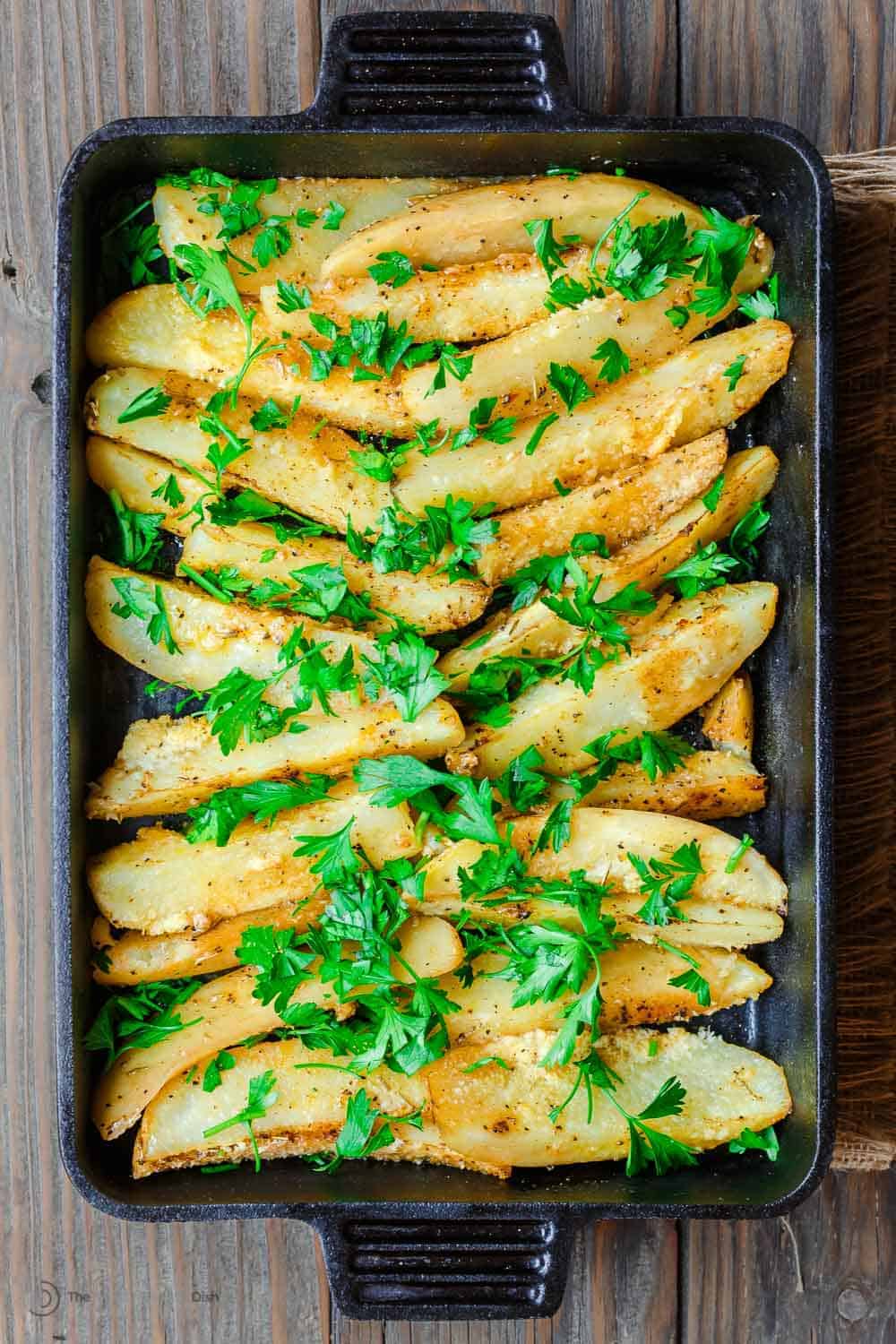 roasted greek potatoes in a baking dish topped with parsley.
