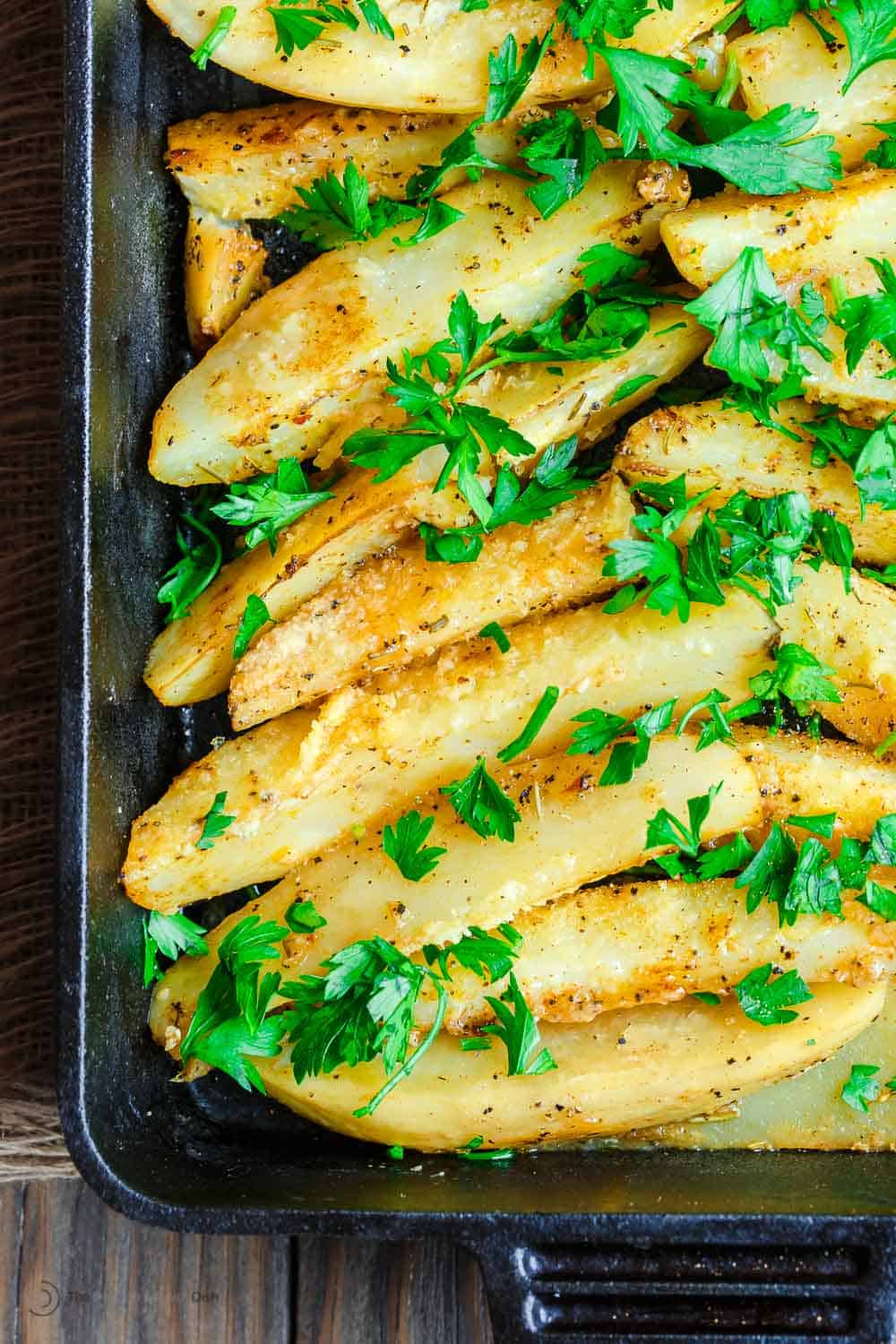 close up of roasted greek potatoes in a baking dish topped with parsley.