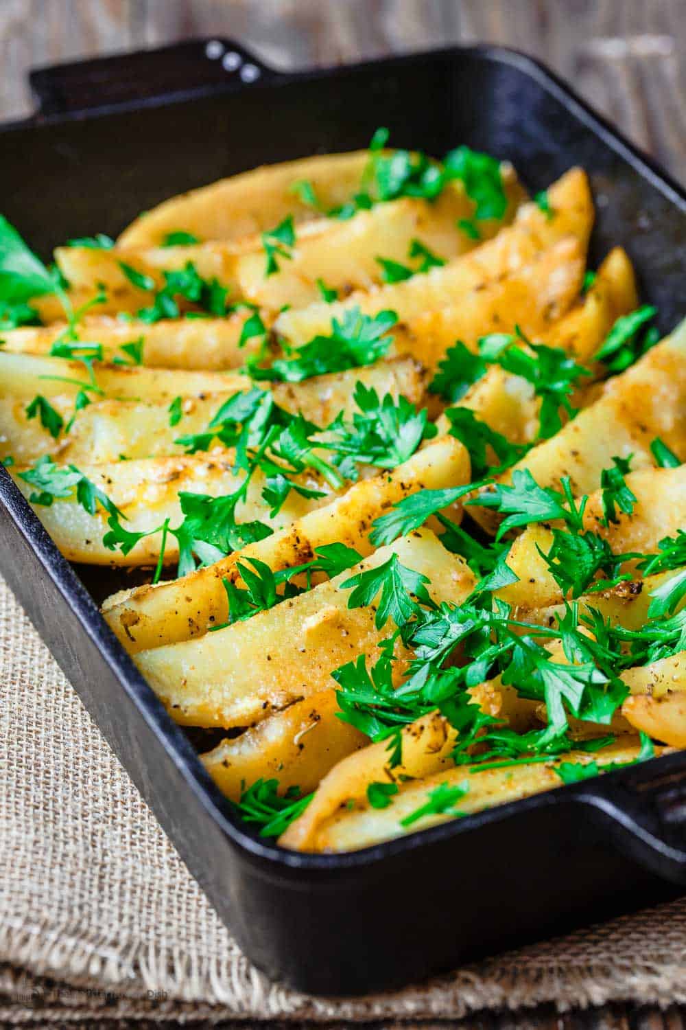close up of roasted greek potatoes in a baking dish topped with parsley.