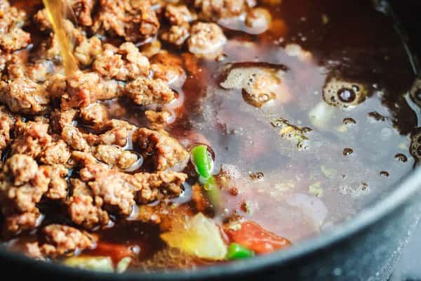 Cooked sausage and broth added to pan of vegetables and spices