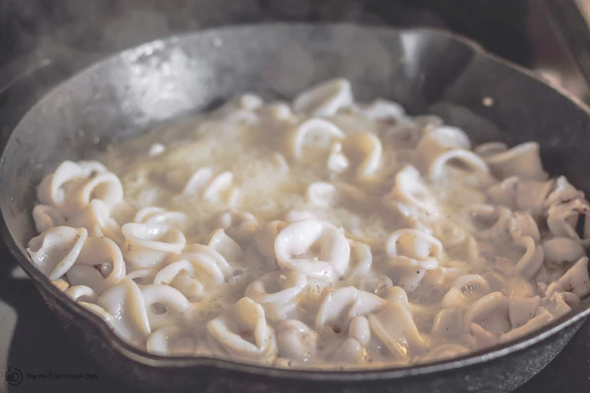 Calamari and garlic cooking in cast iron skillet