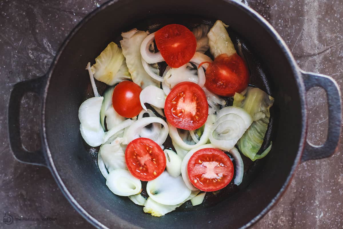 Layer of sliced onions, tomatoes and cabbage leaves on bottom of large pot