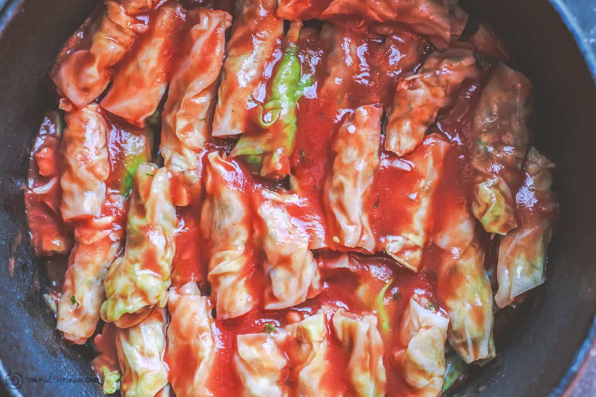 Vegetarian stuffed cabbage rolls layered in large pot with tomato sauce