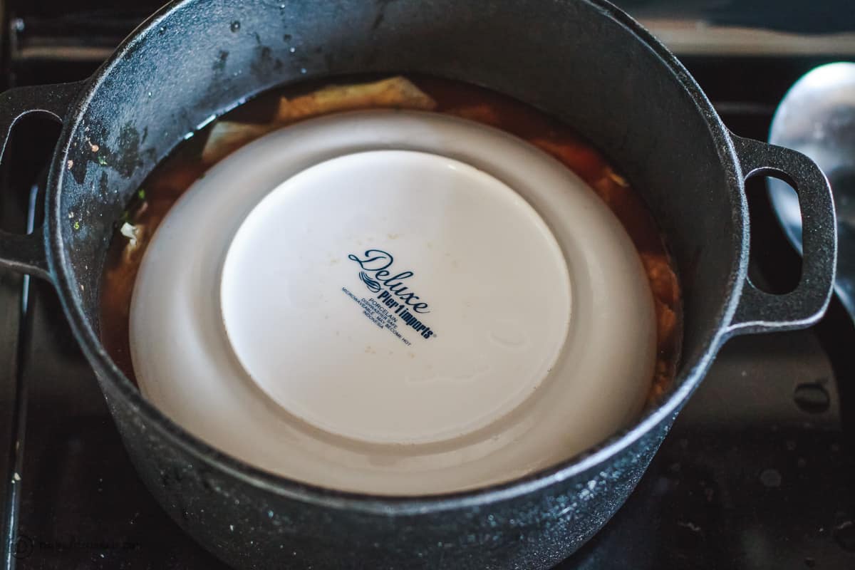 Vegetarian stuffed cabbage rolls cooking in large pot with plate setting on top