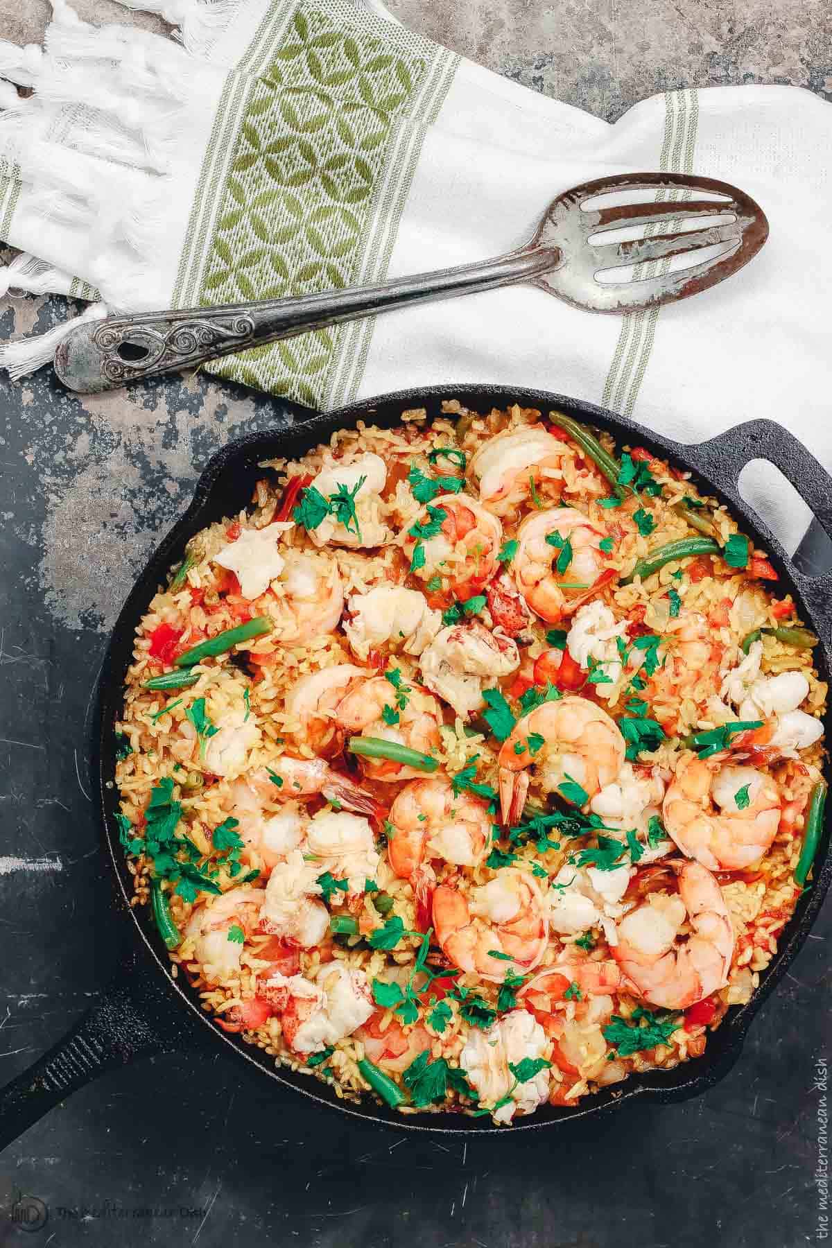 Seafood paella in a cast iron skillet with a large serving spoon