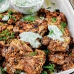 grilled chicken thighs served on a tray with dill yogurt sauce on top