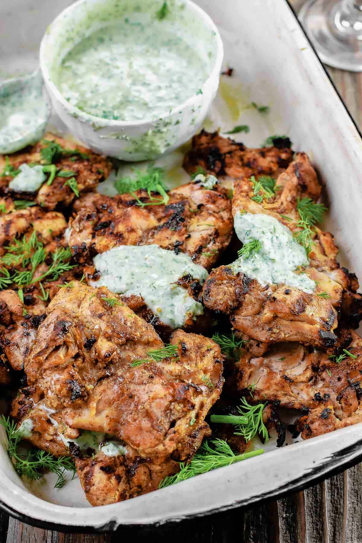 grilled chicken thighs served on a tray with dill yogurt sauce on top