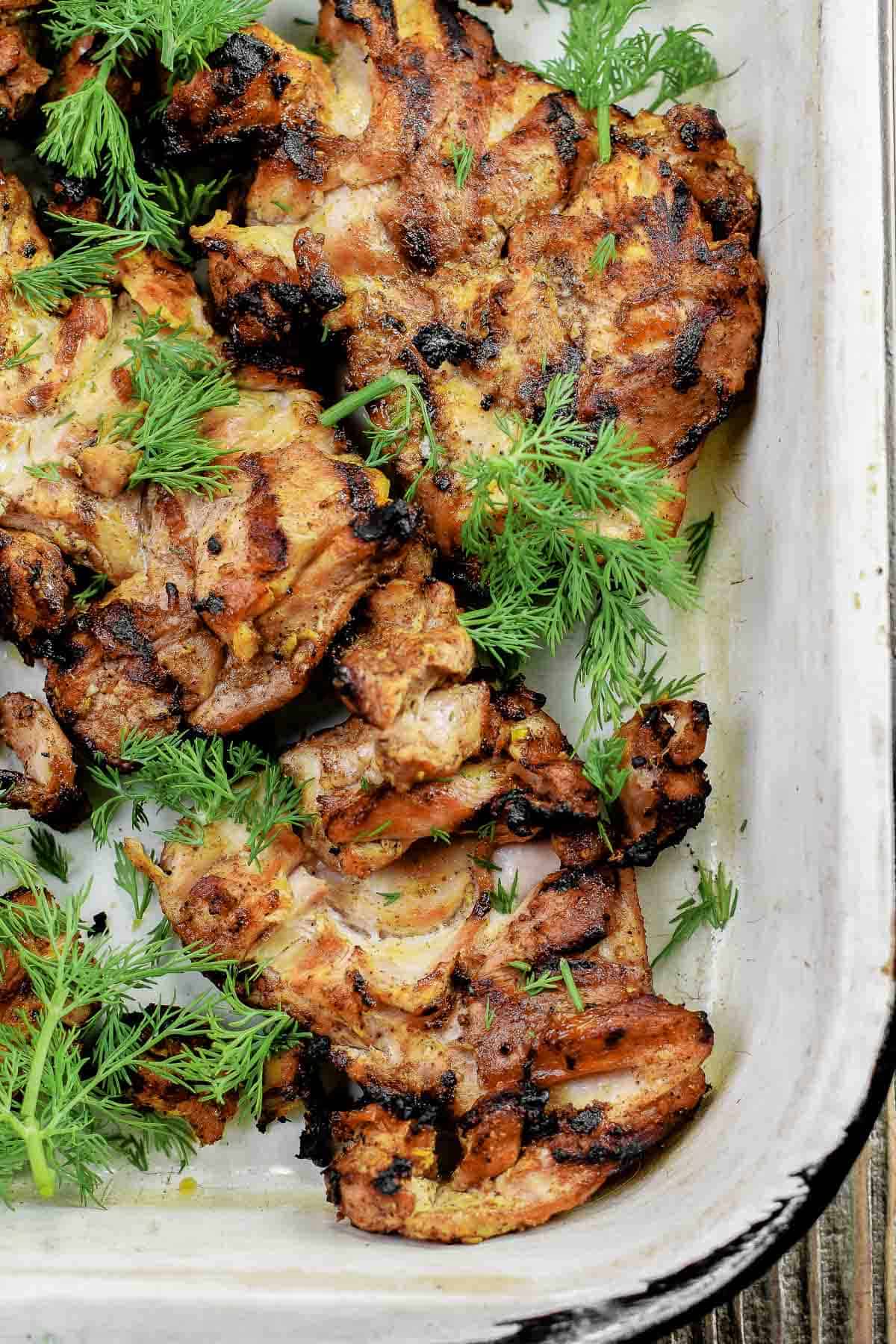 Grilled chicken pieces in a white tray, garnished with fresh dill