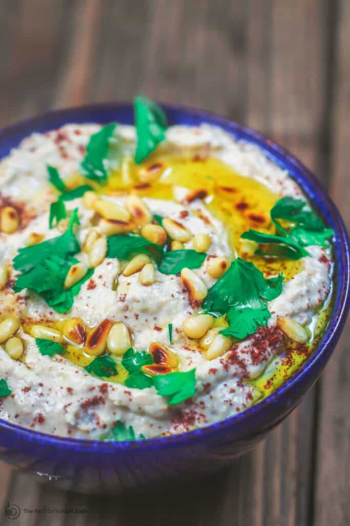 Baba ganoush in a bowl topped with parsley, toasted pine nuts, sumac and olive oil.