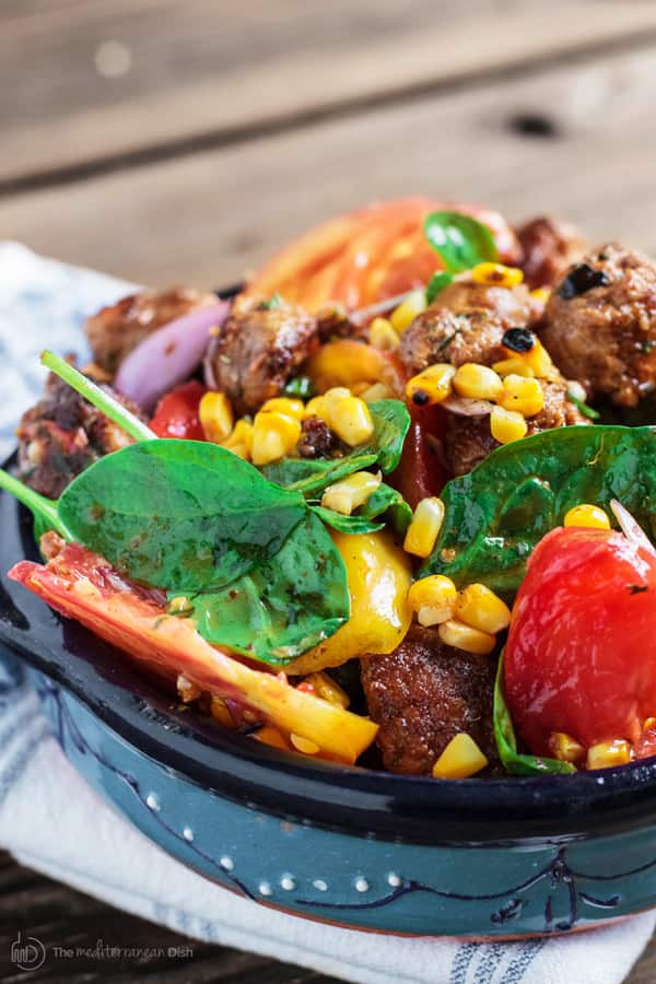 Spinach salad garnished with corn, tomatoes and chorizo