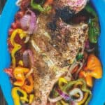 Roasted whole red snapper placed on a bed of vegetables in a dish