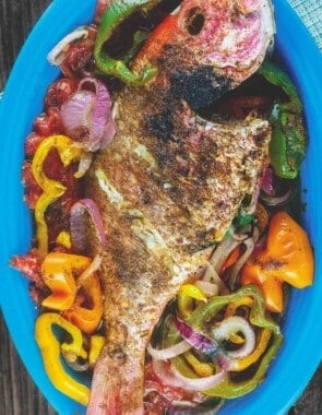 Roasted whole red snapper placed on a bed of vegetables in a dish