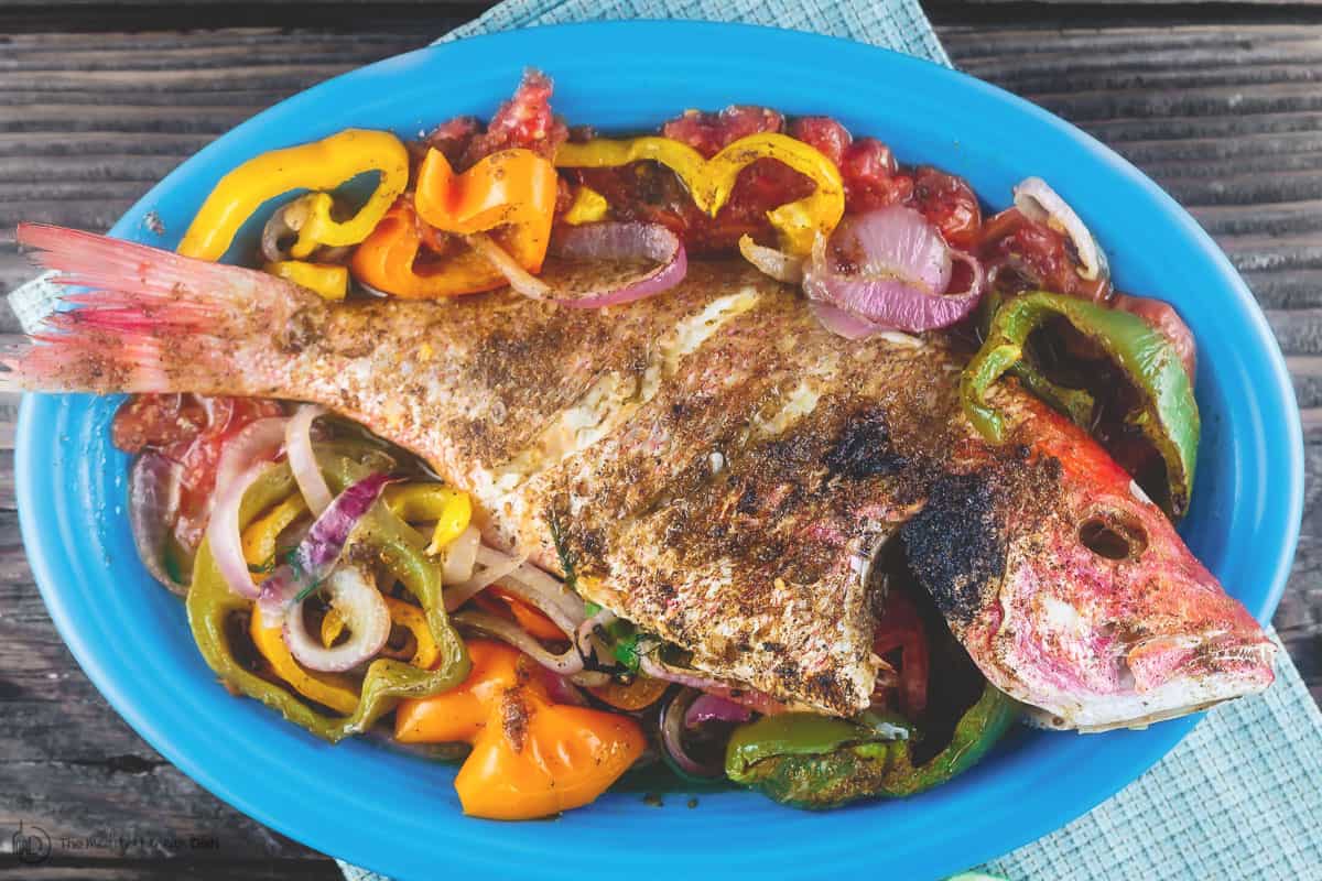 Roasted whole red snapper with vegetables served on a large dish