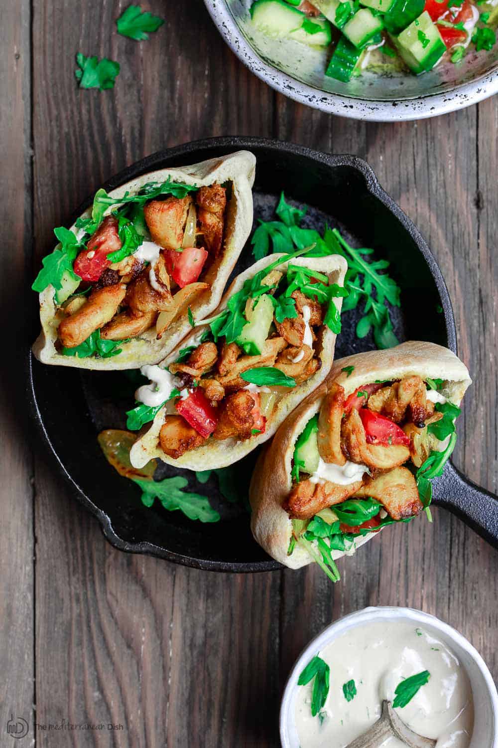 Chicken shawarma in pita pockets, served next to a side of tahini and Mediterranean salad