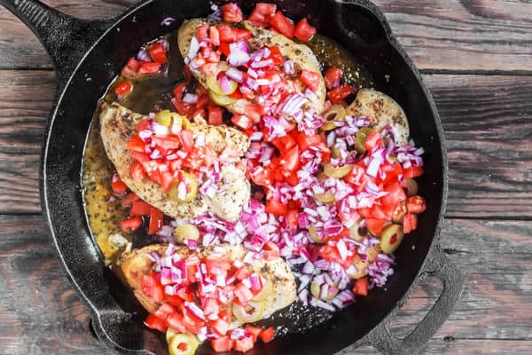 Tomatoes and onions added to skillet on top of chicken breasts