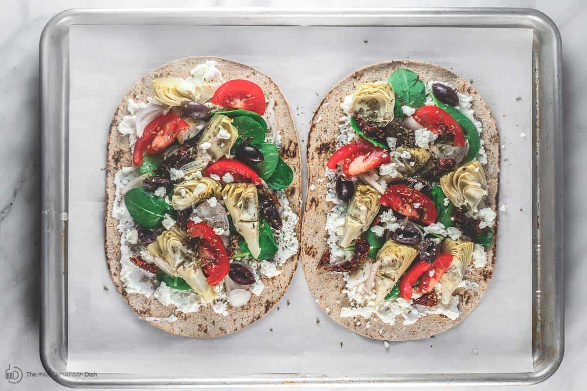 Flatbread pizza with feta cheese and garden vegetables on baking sheet