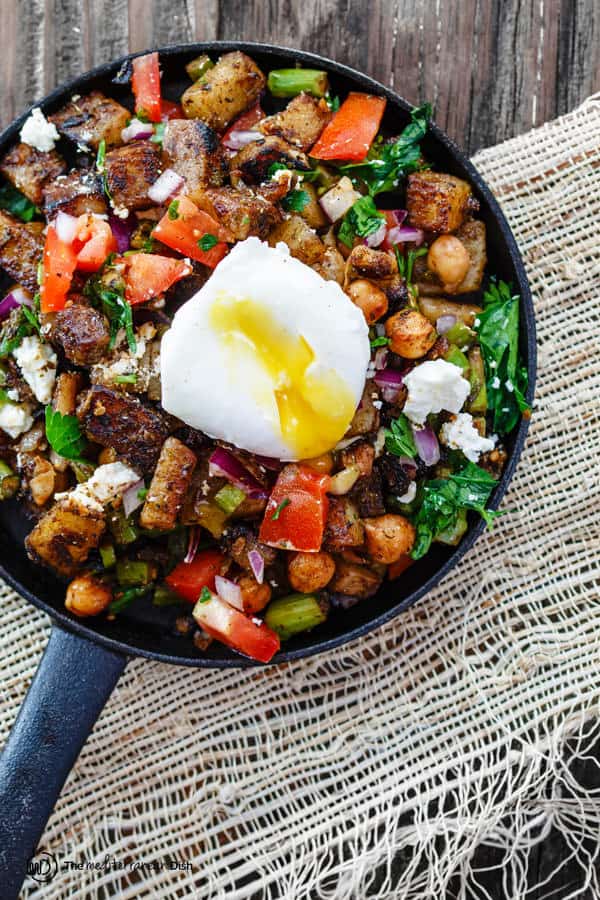 Mediterranean Potato Hash in skillet with toppings and broken poached egg