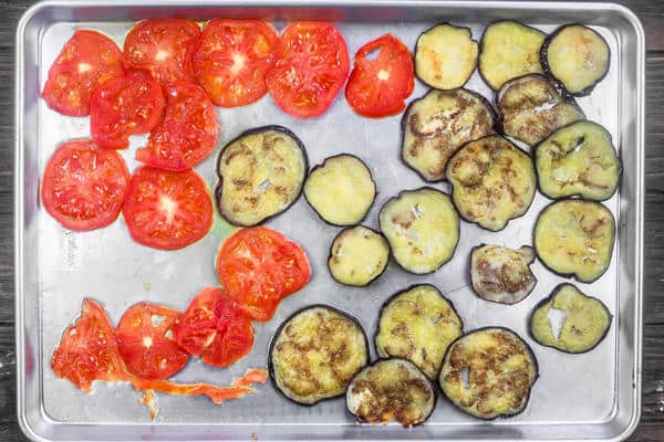 Slices of eggplant and tomatoes lined on a baking sheet