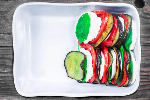 Eggplant, tomatoes and cheese slices placed in a baking dish