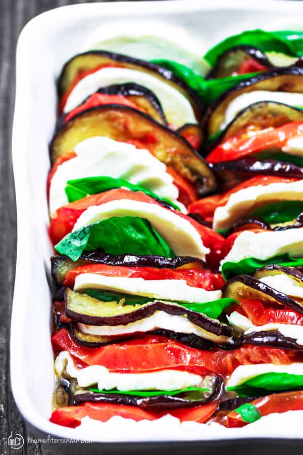 Slices of Roasted Eggplant, Mozzarella cheese and tomatoes lined up in a dish, garnished with fresh basil
