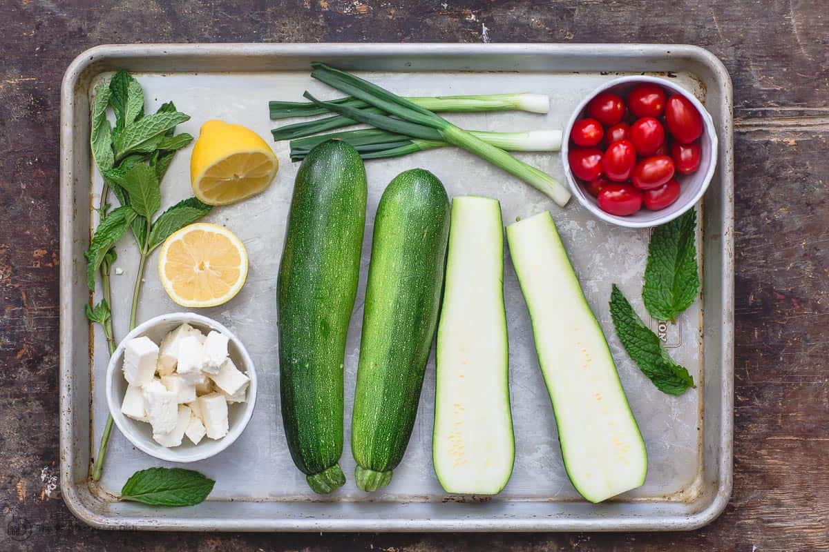 Ingredients for zucchini boats including zucchini, feta, cherry tomatoes, fresh herbs, green onions, and lemon