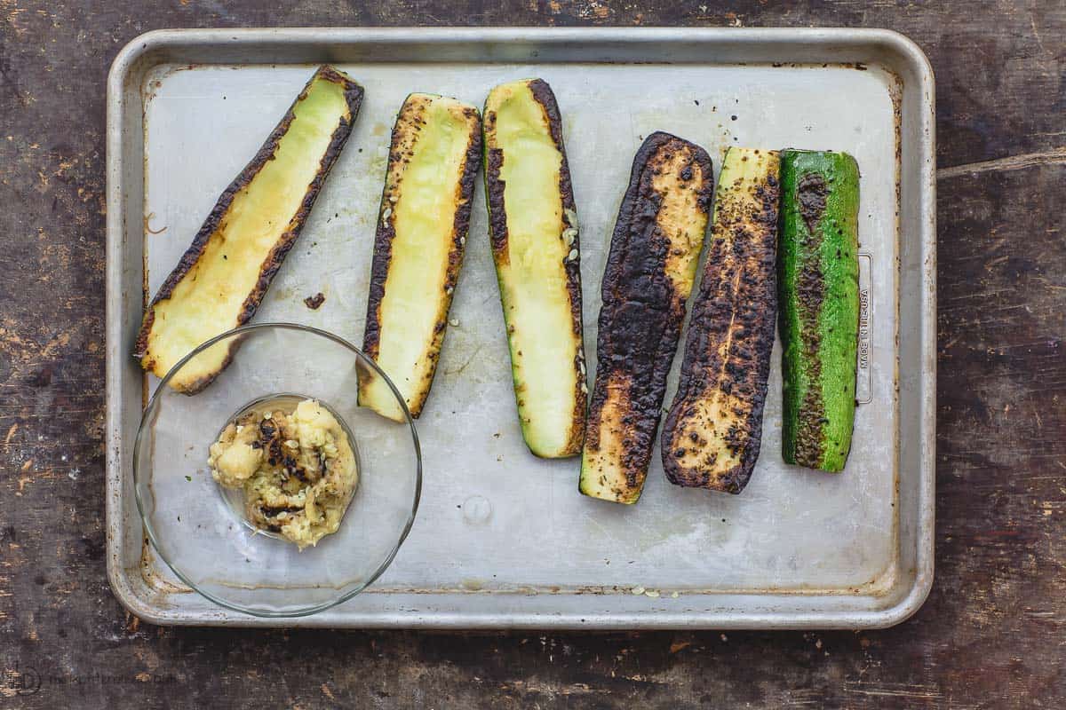 Grilled zucchini halves. Some zucchini flesh scooped out on the side to make zucchini boats