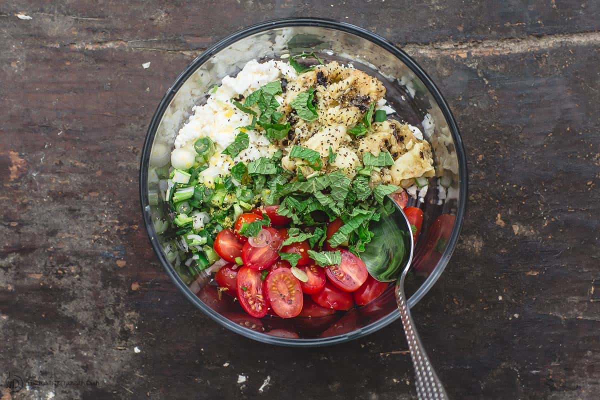 Zucchini boat filling. A bowl of sliced cherry tomatoes, zucchini flesh from grilled zucchini, feta, fresh herbs, and chopped green onions