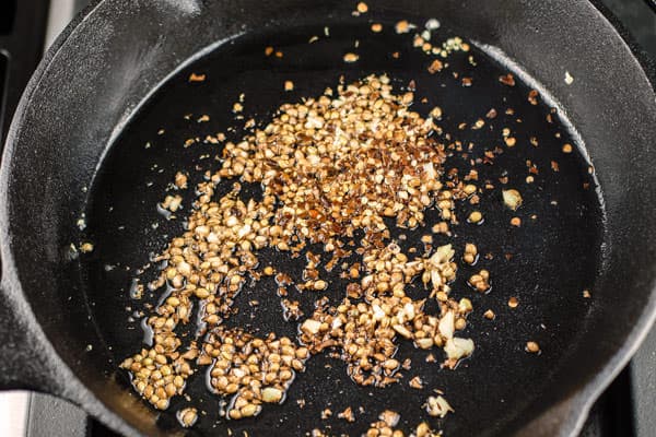Minced garlic, red pepper flakes, and coriander seeds cooking in olive oil