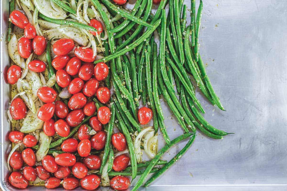 green beans, cherry tomatoes, and a sliced yellow onion on one side of a sheet pan.