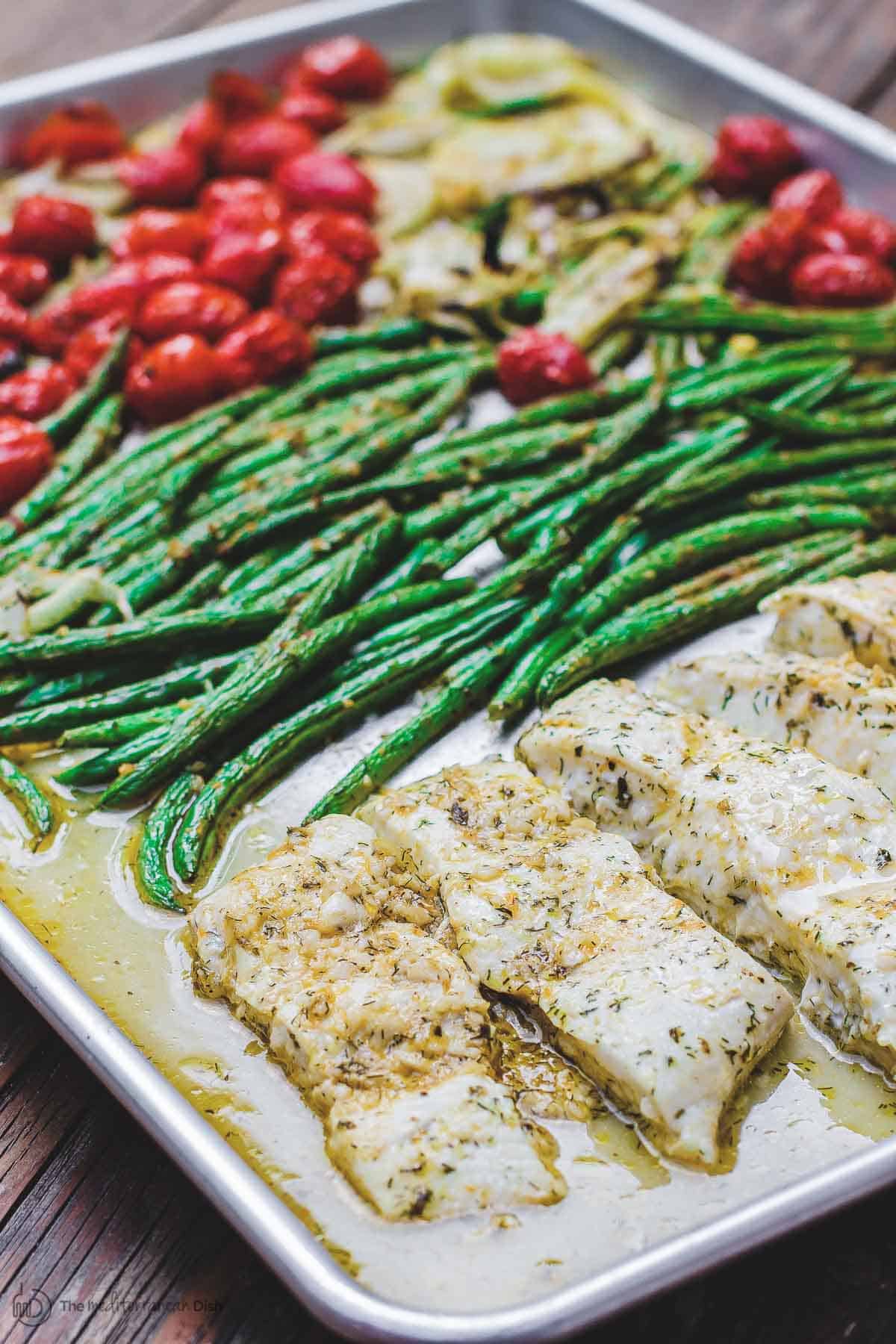 Halibut recipe with green beans, tomatoes, and onion, all tossed in a Mediterranean sauce and then baked on a sheet pan. 