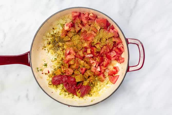 Skillet filled with diced onion, jalapenos, garlic and tomatoes, mixed with spice mix