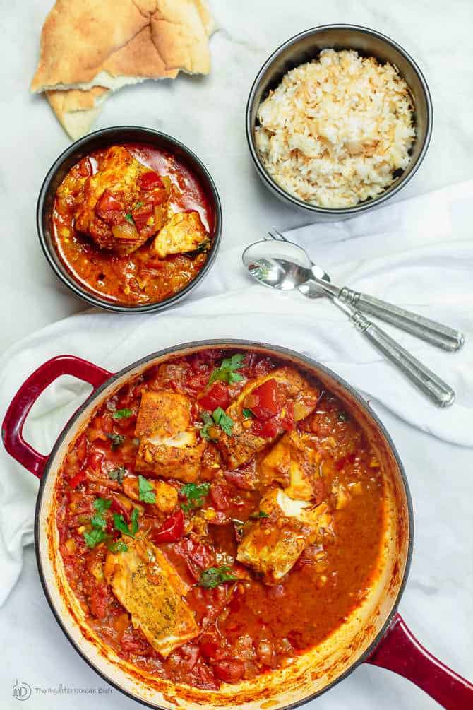 Cod fish fillet cooked with tomato sauce in braiser, served next to a bowl or rice