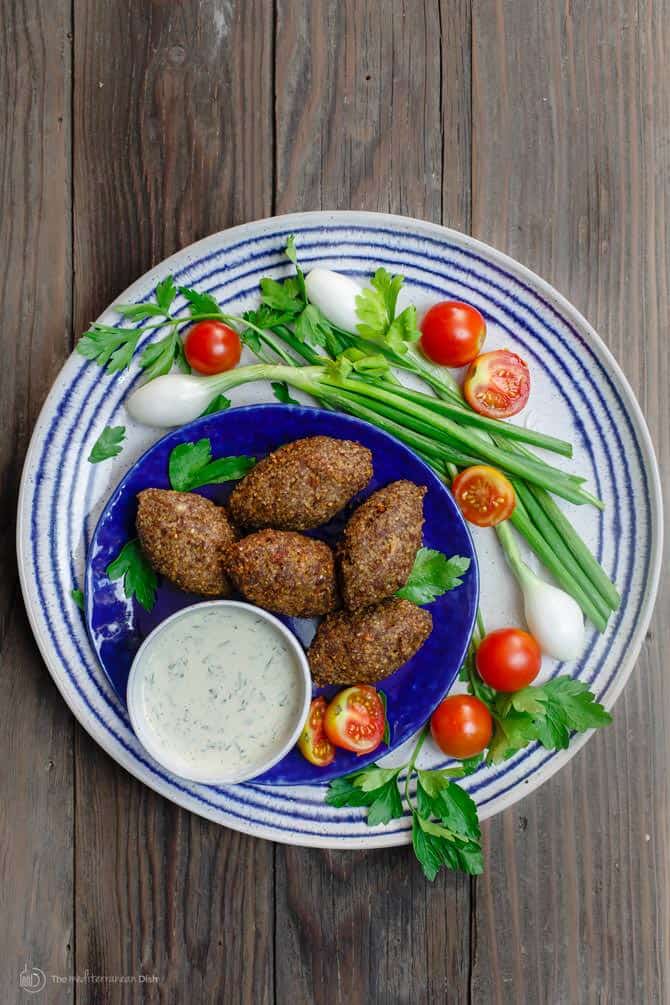 5 pieces of Kibbeh served on a plate with dip and vegetables