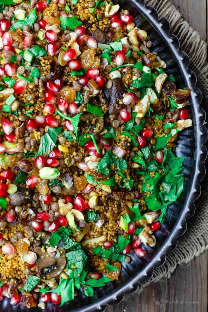 Colorful couscous dish with bright red pomegranate seeds, hearty mushrooms, nuts and garnished with parsley.