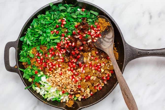 Skillet containing all ingredients of dish. Very colorful garnished with pomegranate seeds, nuts, parsley and scallions.