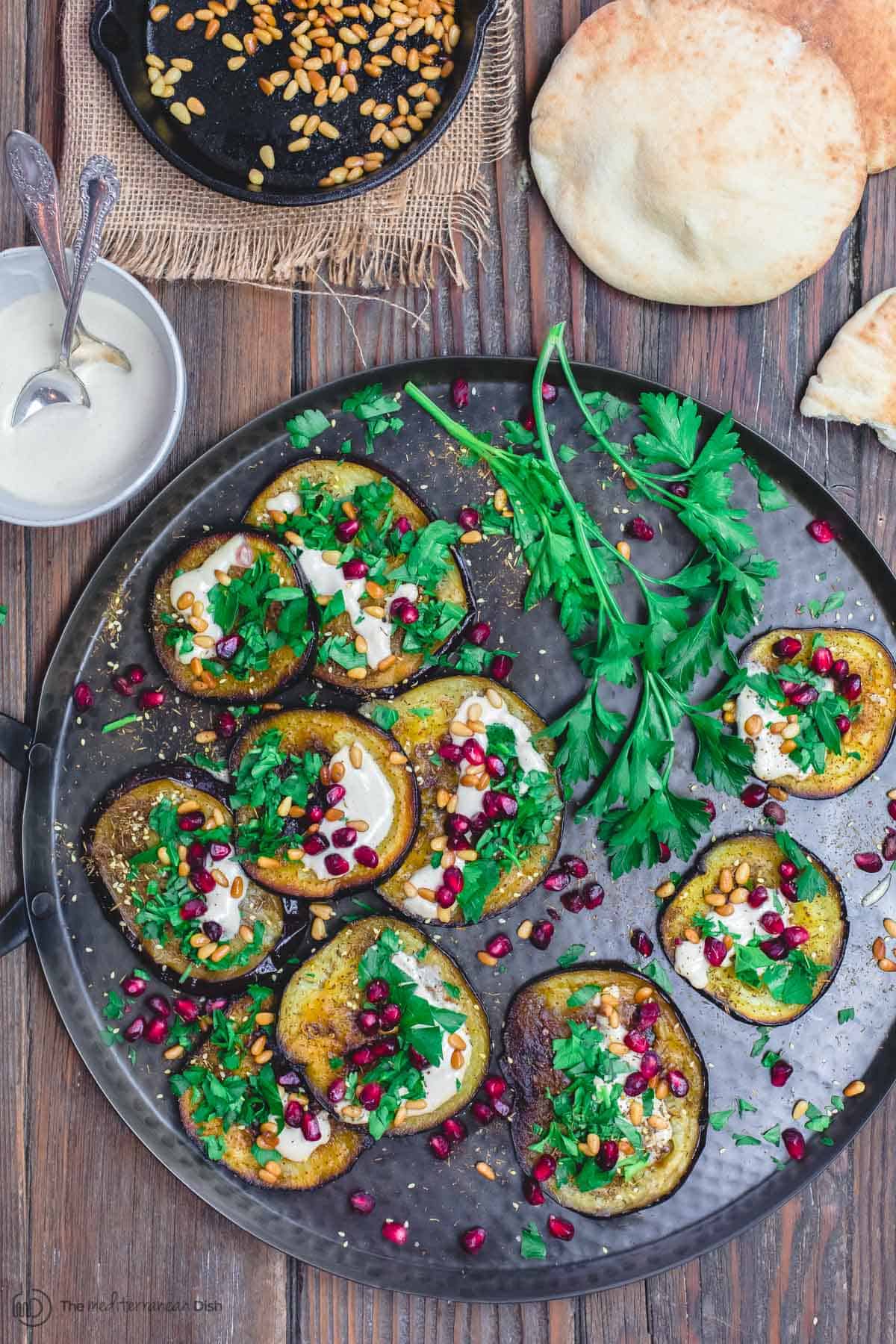 Mediterranean Roasted Eggplant Recipe | The Mediterranean Dish. An easy roasted eggplant recipe, prepared Mediterranean-style with pomegranates, tahini and fresh parsley. Great as an appetizer, salad, or side dish! See it on TheMediterraneanDish.com