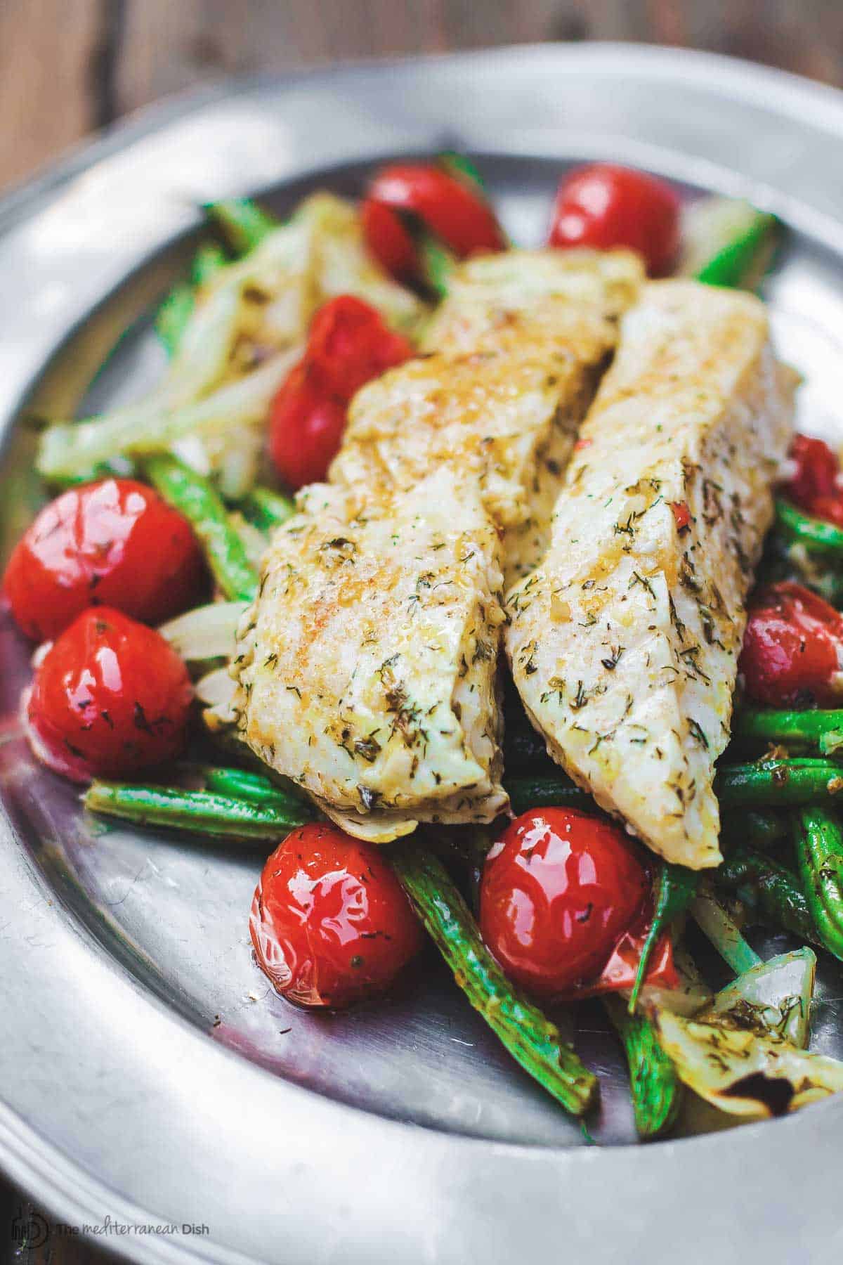 Baked halibut served on a plate with tomatoes and green beans.