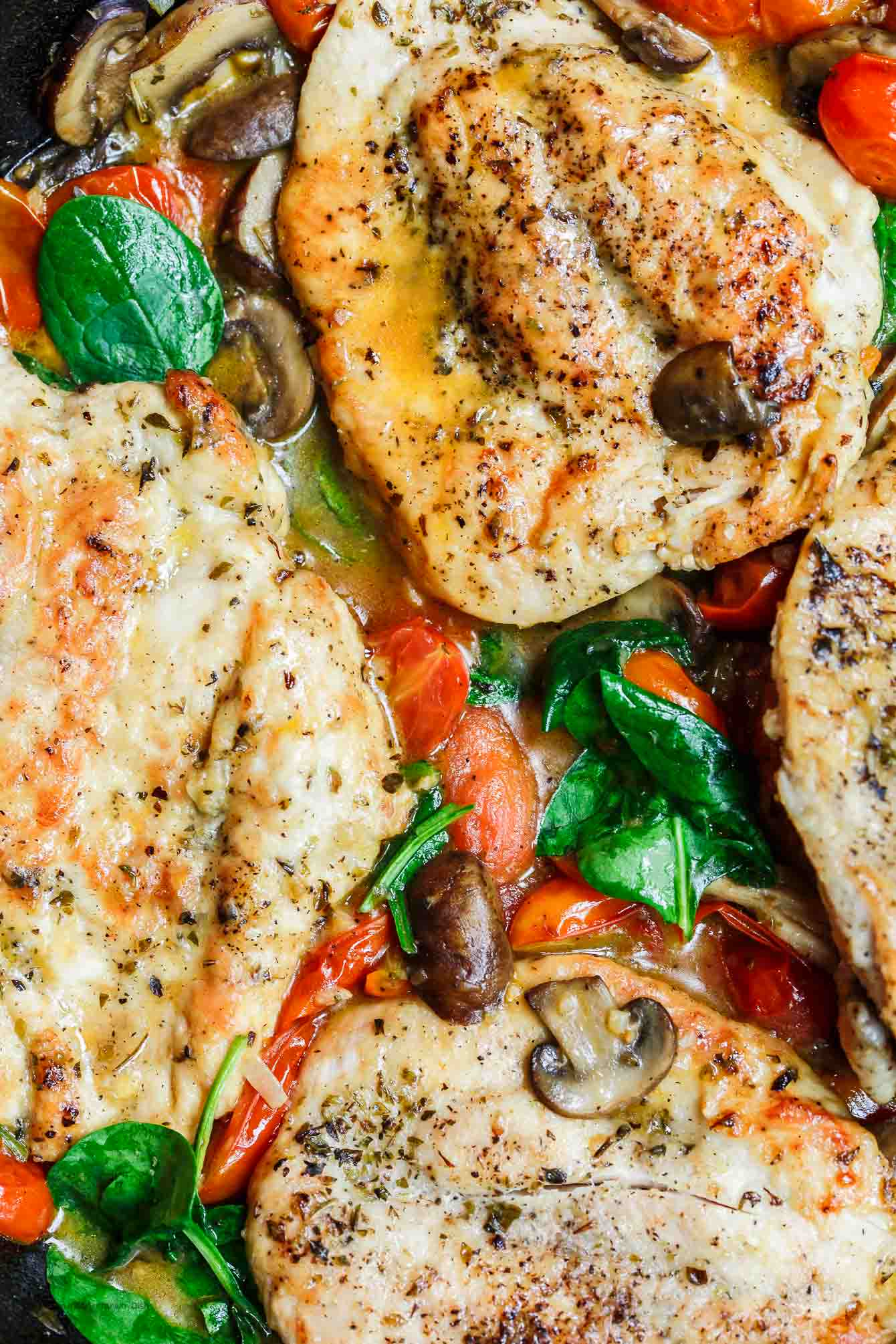 Close up of chicken cutlets in a skillet with tomatoes and spinach
