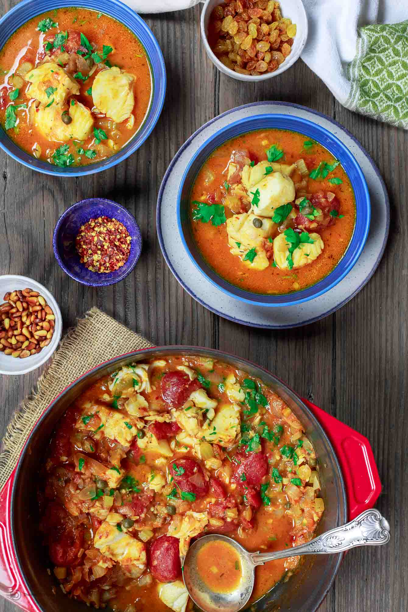 Fish stew served in bowls with extra red pepper and raisins on side