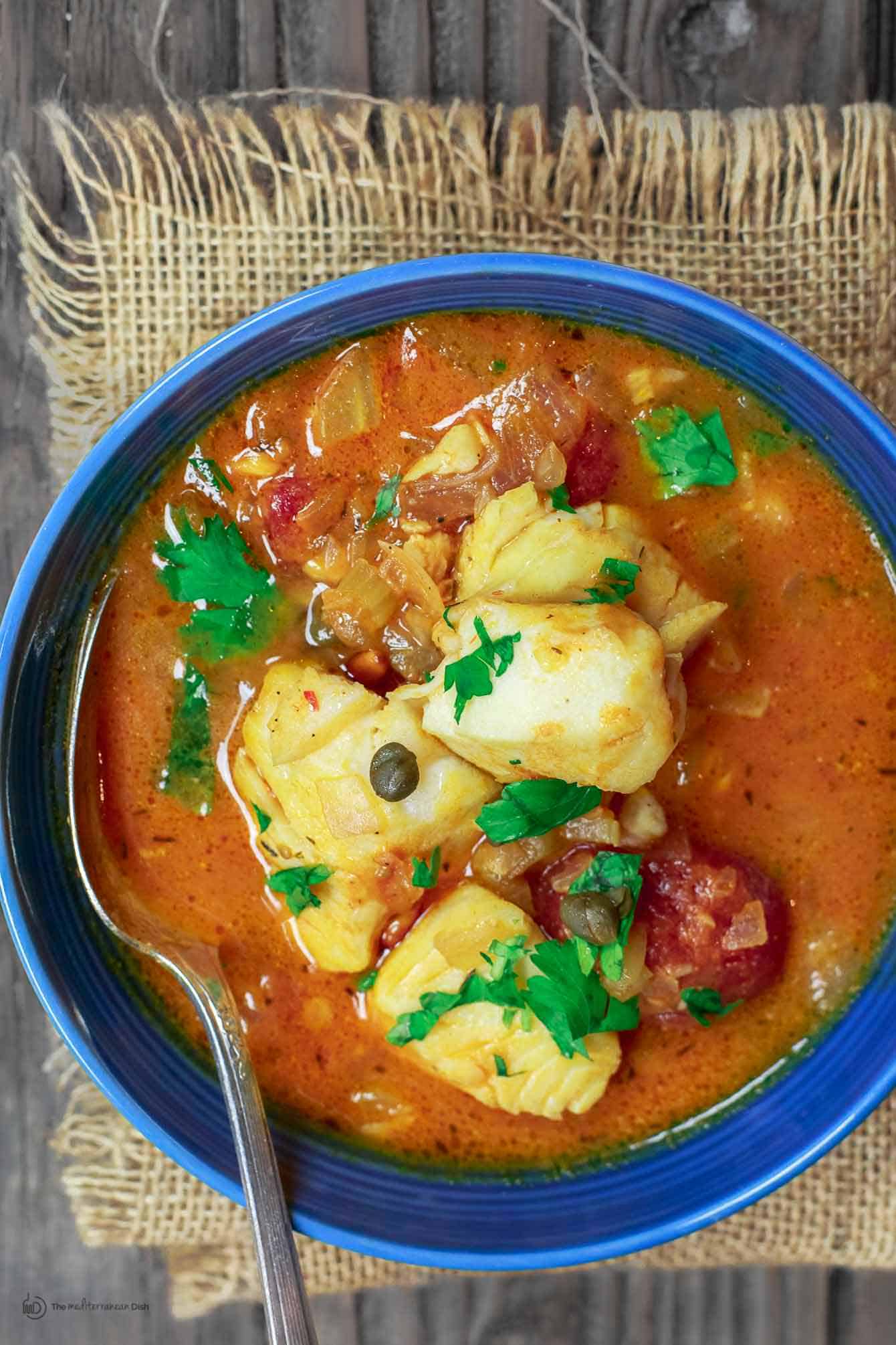 Close-up of fish stew garnished with pine nuts and parsley