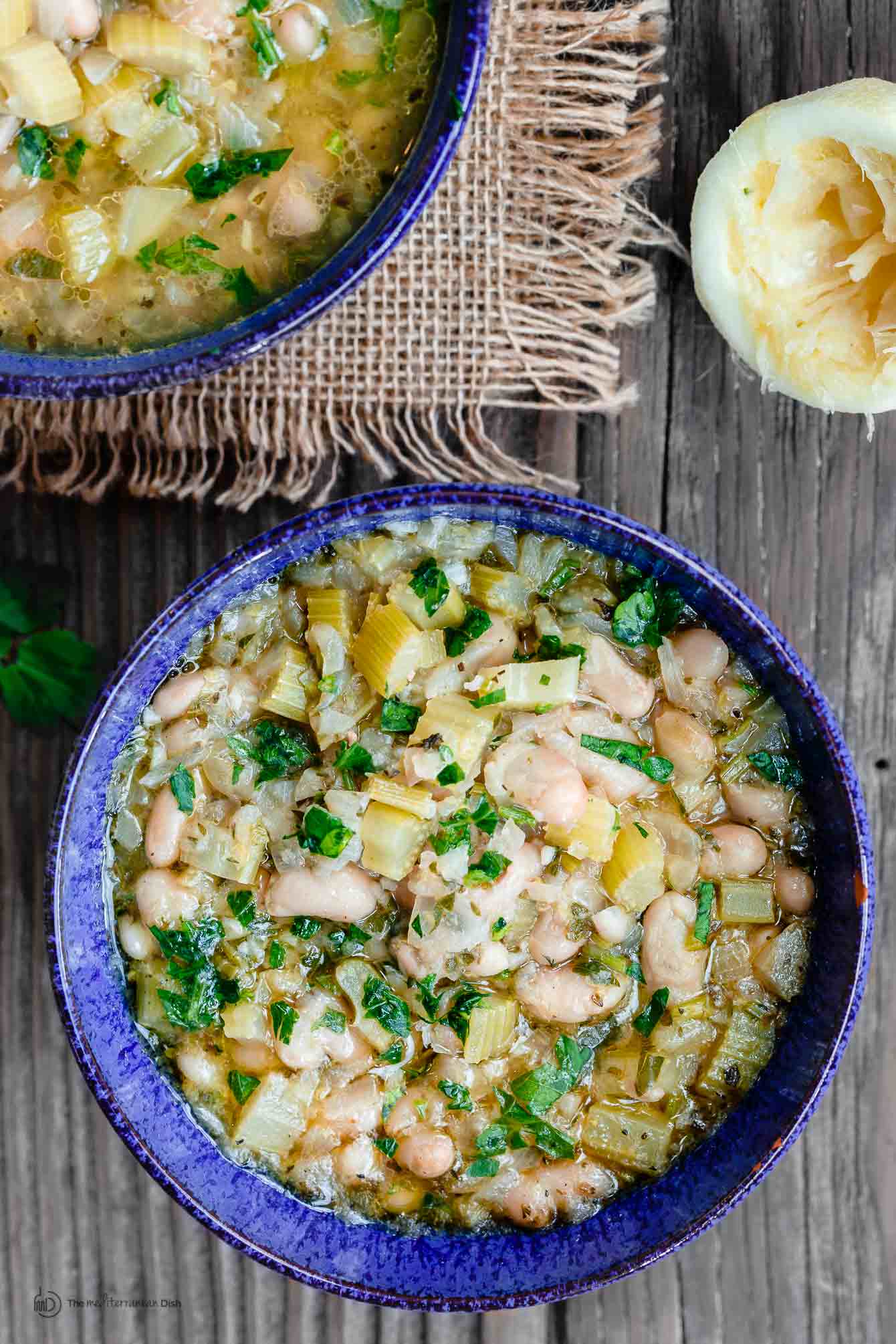 Two bowls of Greek Bean Soup garnished with fresh parsley