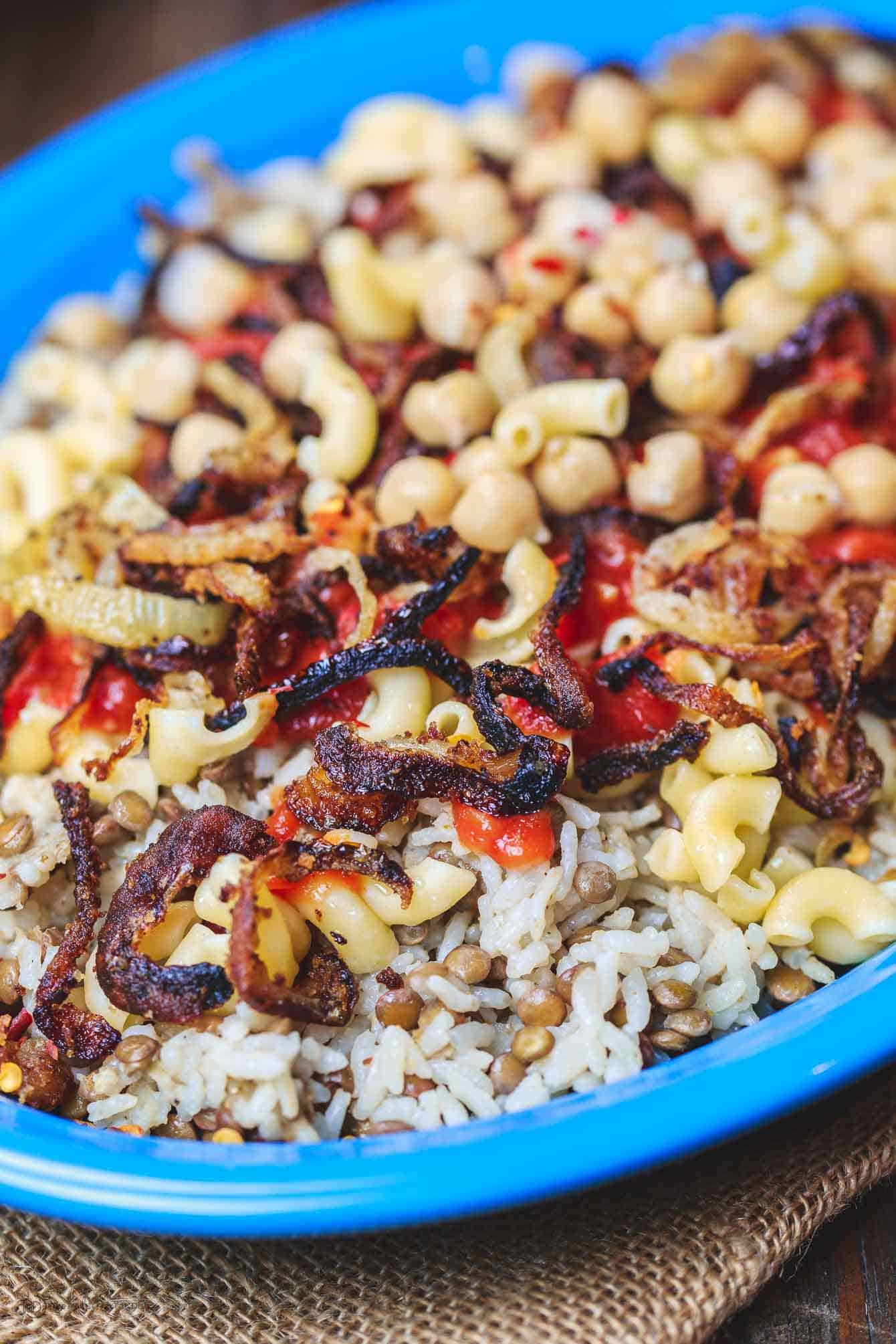 Egyptian Koshari Recipe | The Mediterranean Dish. Hands down a family favorite. A comforting bowl of spiced lentils and rice with chickpeas, tiny pasta, and tomato sauce. Topped with thin crispy onion rings. A tasty, budget friendly, vegan recipe! See it on TheMediterraneanDish.com