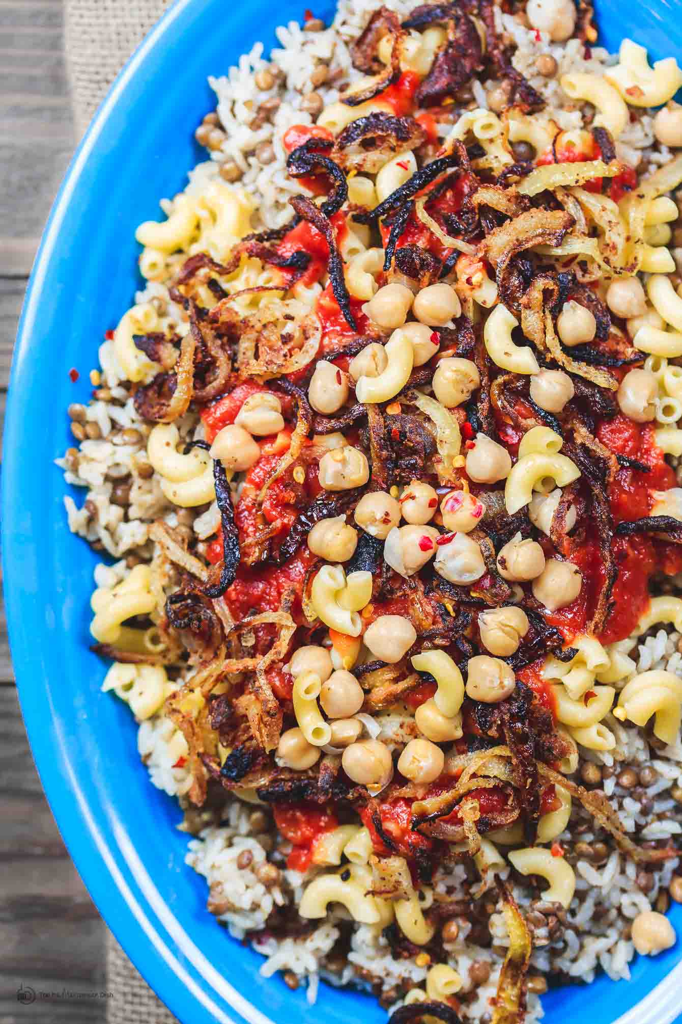 Egyptian Koshari Recipe | The Mediterranean Dish. Hands down a family favorite. A comforting bowl of spiced lentils and rice with chickpeas, tiny pasta, and tomato sauce. Topped with thin crispy onion rings. A tasty, budget friendly, vegan recipe! See it on TheMediterraneanDish.com