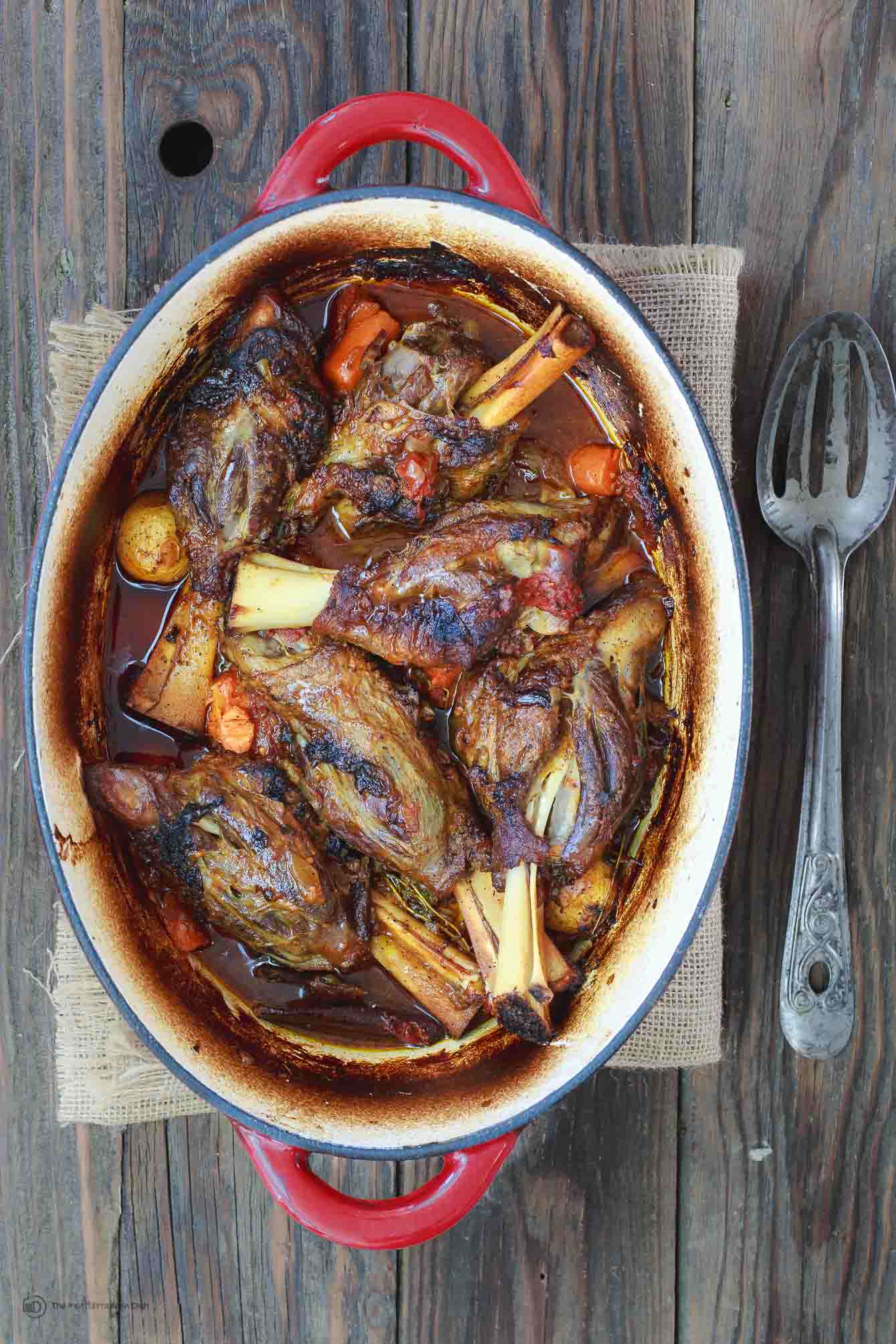 Mediterranean-Style Wine Braised Lamb Shanks Recipe | The Mediterranean Dish. Braising and slow cooker instructions included! Spiced lamb shanks cooked in a red wine and tomato sauce with vegetables, aromatics and fresh herbs! A family favorite for Easter or your next special dinner! See it on TheMediterraneanDish.com