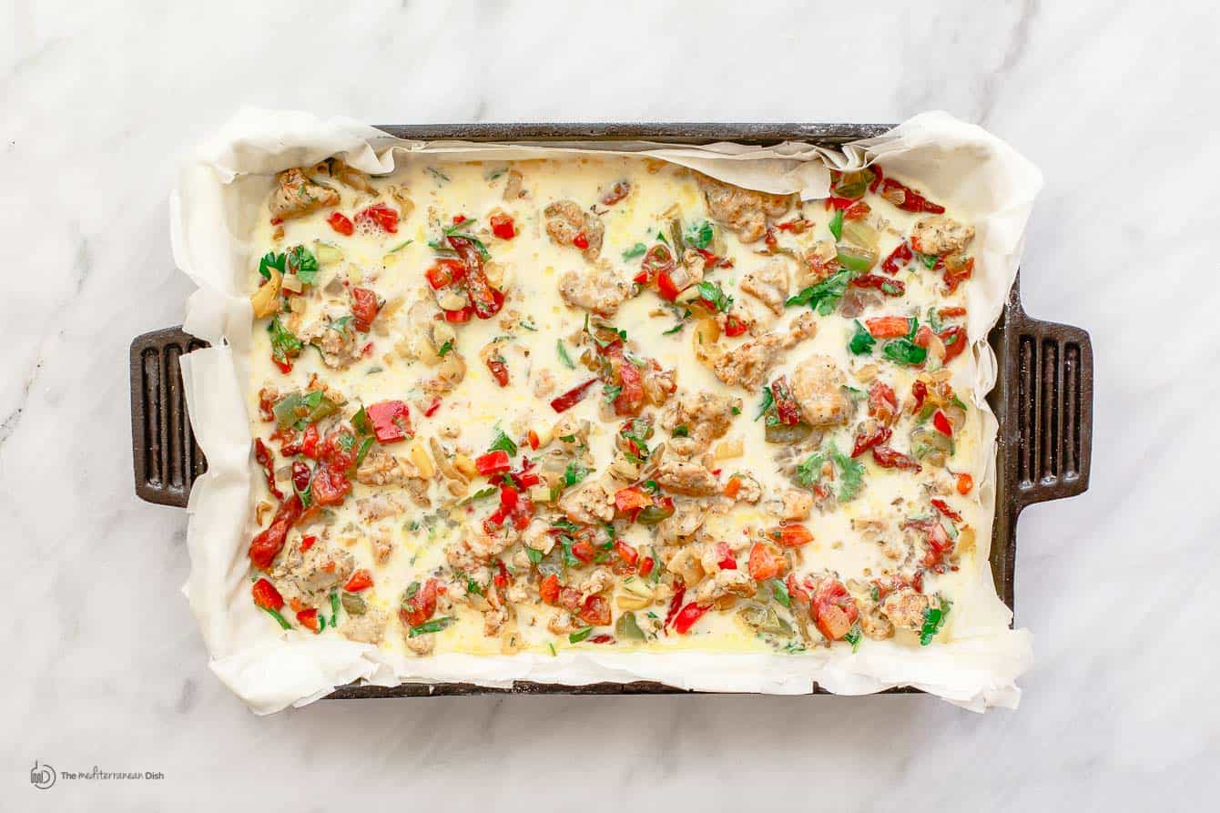Eggs and milk mixture poured over vegetable and sausage mix in baking pan