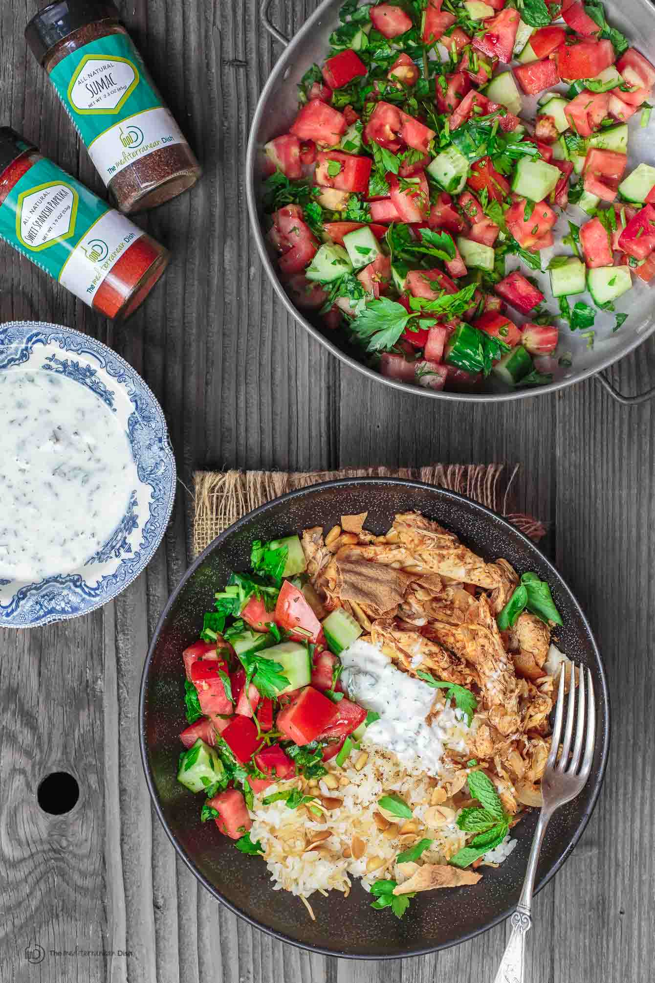 Tomato and cucumber salad with mint dip on the side and bottles of spices on the table